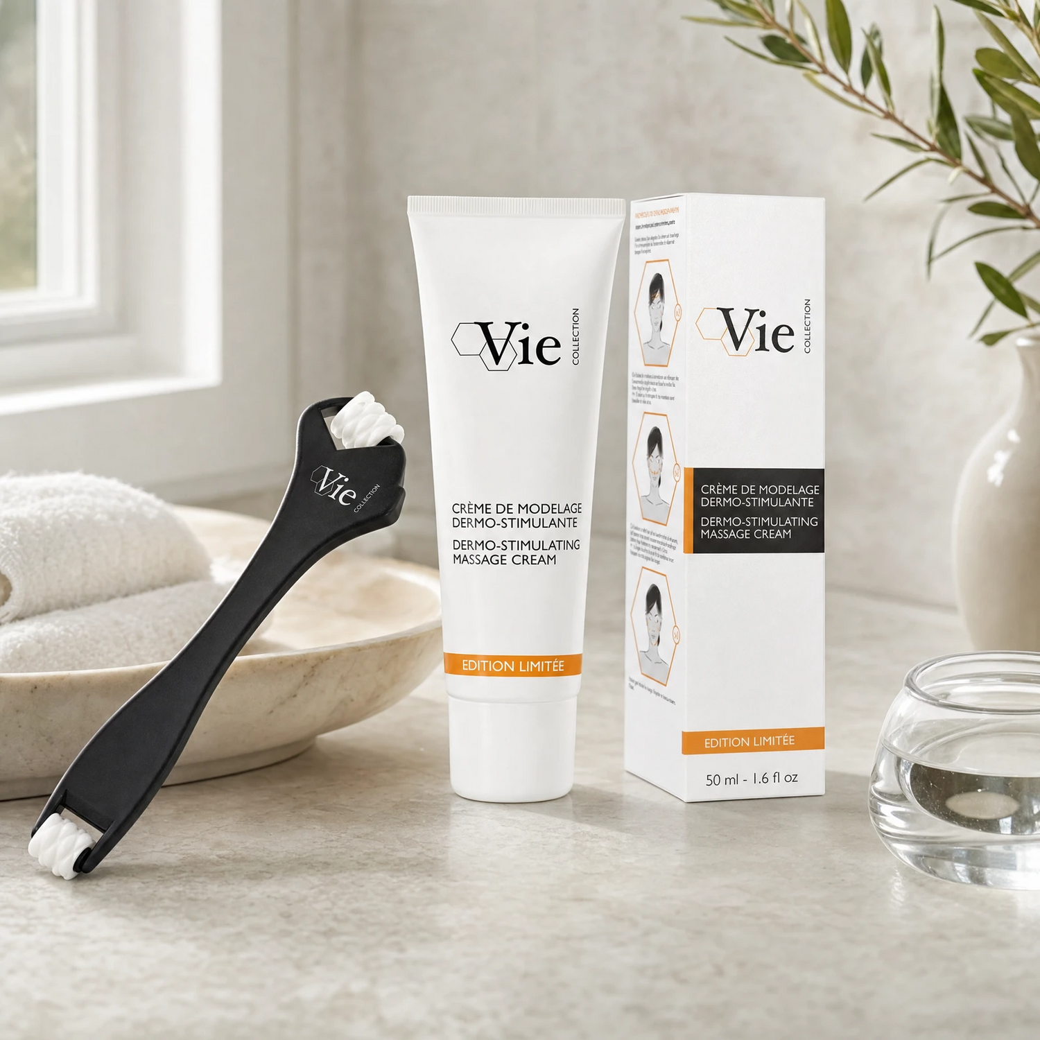 Vie Collection Dermo-Stimulating Massage Cream 50ml Limited Edition with facial roller applicator and retail box on a marble counter with olive branch in white vase, marble bowl with towels and soft window light, premium at-home skincare setting