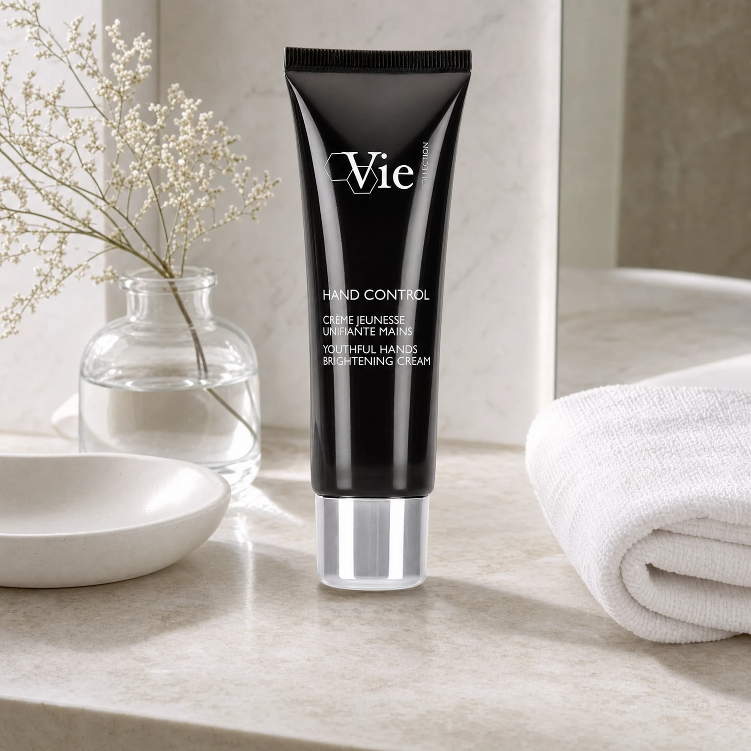 Vie Collection Hand Control Youthful Hands Brightening Cream 50ml on a limestone bathroom counter with gypsophila in glass carafe, white ceramic dish, white waffle towel and round mirror, premium at-home skincare setting