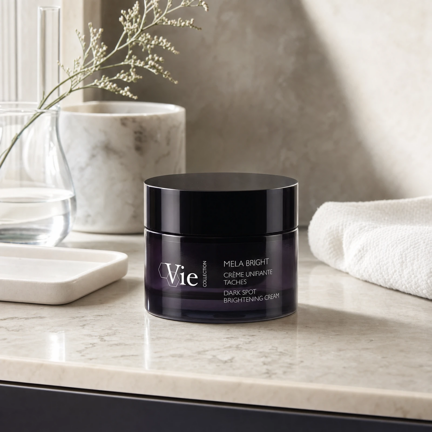 Vie Collection Mela Bright Dark Spot Brightening Cream 50ml on a marble bathroom counter with gypsophila in glass carafe, marble canister, white ceramic tray, white waffle towel and dark cabinetry in background, premium at-home skincare setting