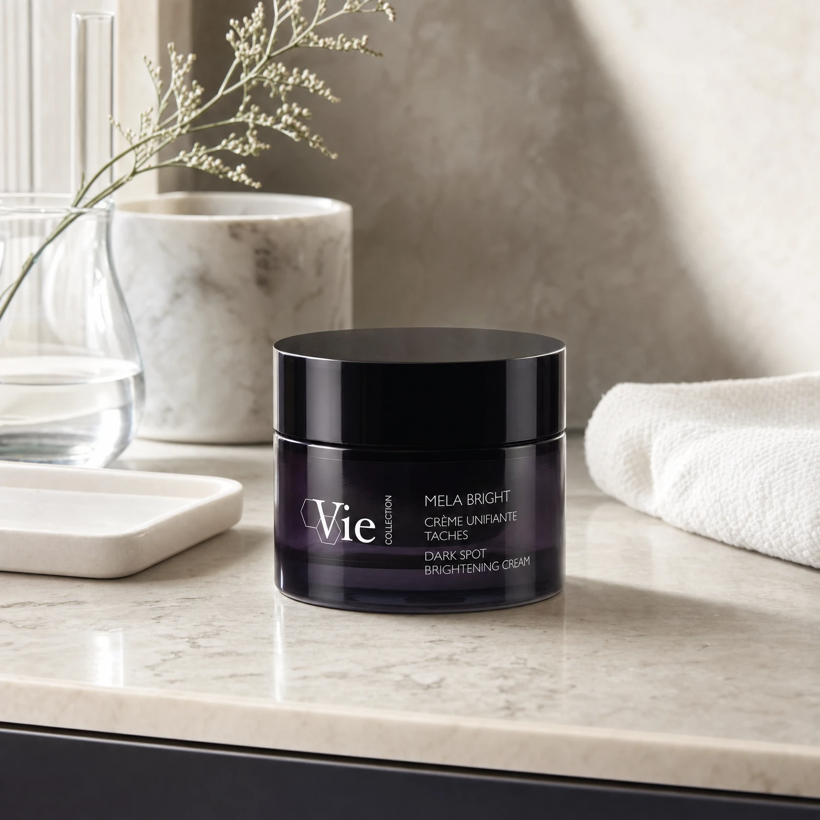 Vie Collection Mela Bright Dark Spot Brightening Cream 50ml on a marble bathroom counter with gypsophila in glass carafe, marble canister, white ceramic tray, white waffle towel and dark cabinetry in background, premium at-home skincare setting
