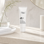 Vie Collection Mela White Protective Sunscreen SPF30 50ml on a marble bathroom counter with gypsophila in glass carafe, white ceramic tray with towel, marble canister and gold round mirror, premium at-home skincare setting