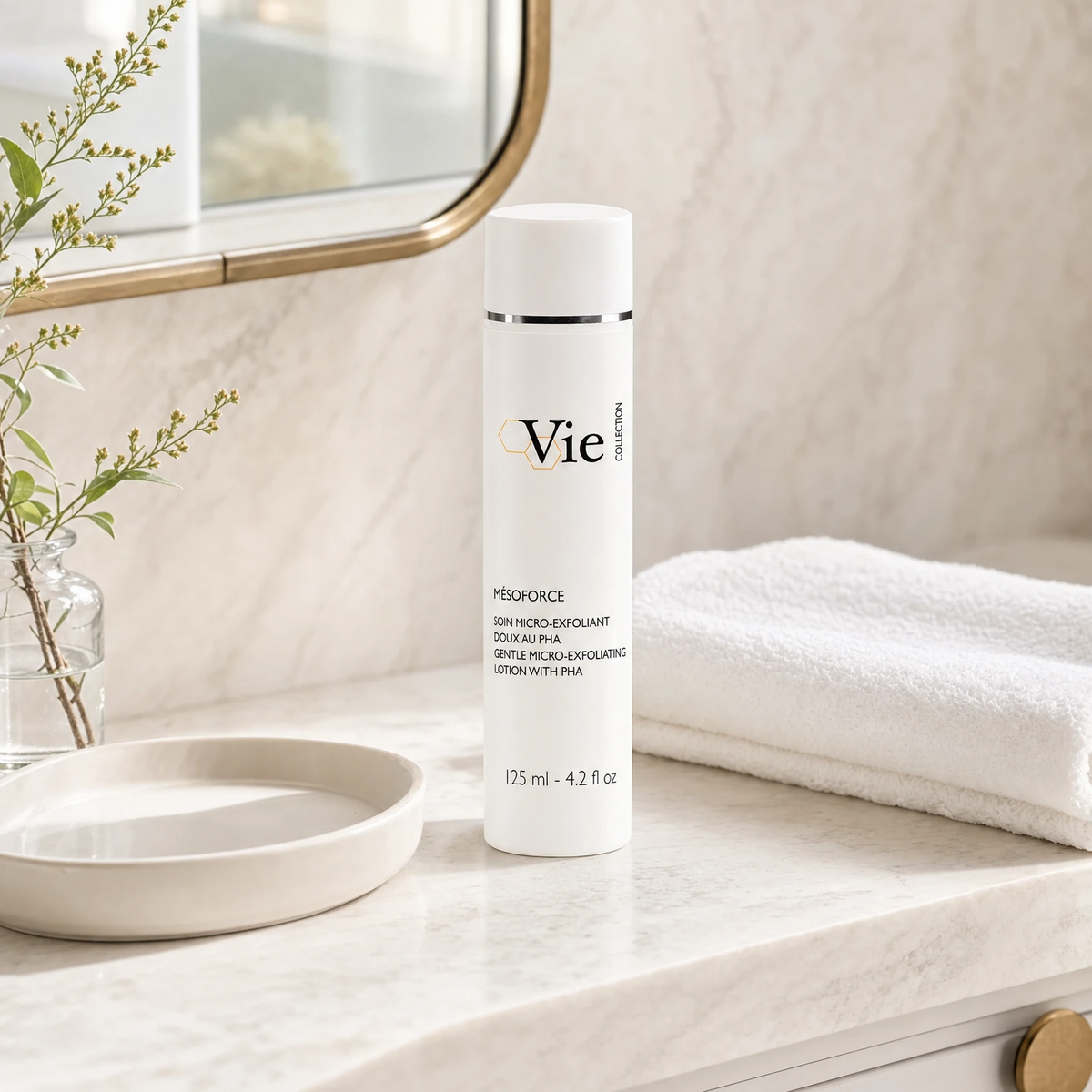 Vie Collection Mésoforce Gentle Micro-Exfoliating Lotion with PHA 125ml on a marble bathroom counter with botanical in glass carafe, round stone tray, stacked white spa towels and gold round mirror, premium at-home skincare setting