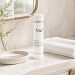 Vie Collection Mésoforce Gentle Micro-Exfoliating Lotion with PHA 125ml on a marble bathroom counter with botanical in glass carafe, round stone tray, stacked white spa towels and gold round mirror, premium at-home skincare setting