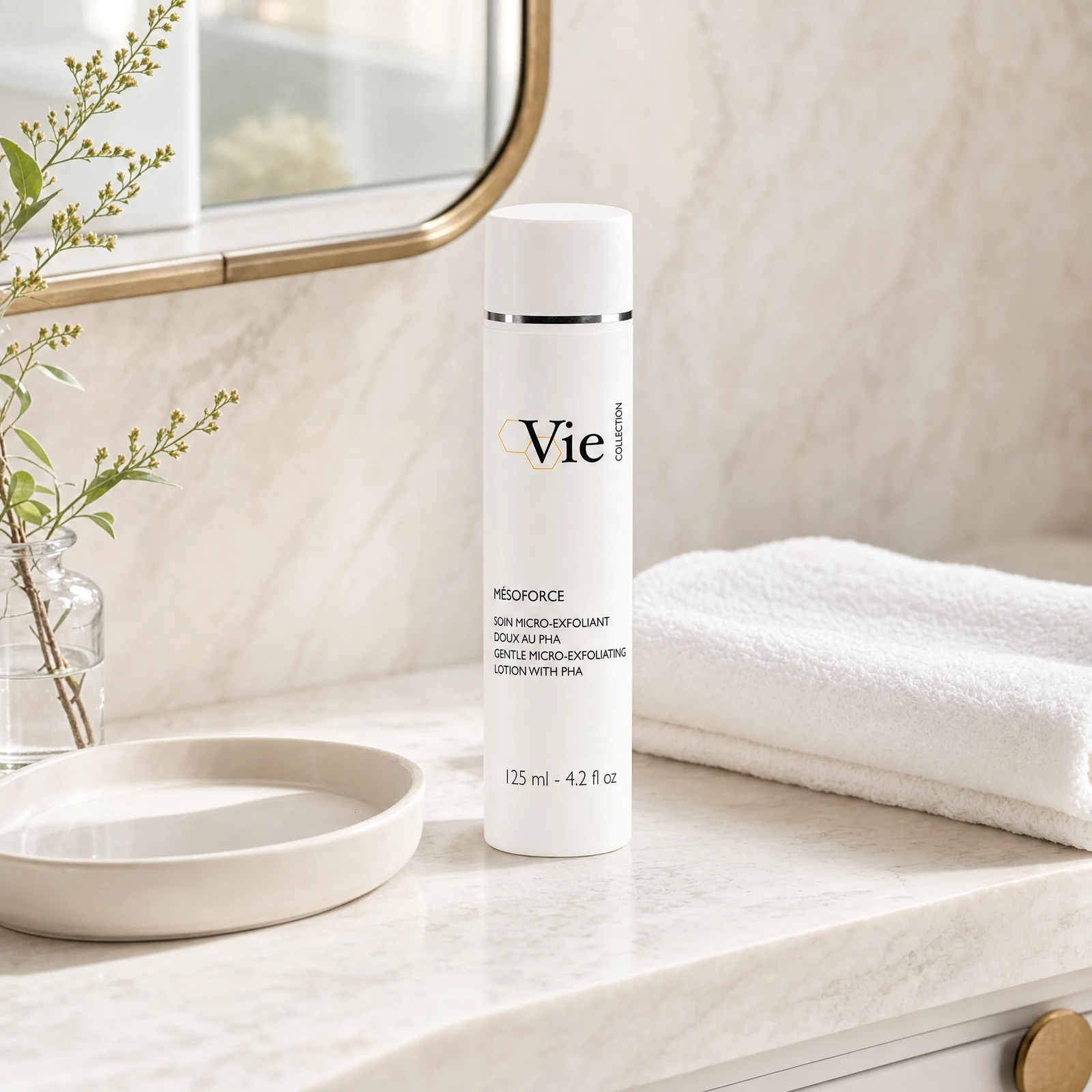 Vie Collection Mésoforce Gentle Micro-Exfoliating Lotion with PHA 125ml on a marble bathroom counter with botanical in glass carafe, round stone tray, stacked white spa towels and gold round mirror, premium at-home skincare setting