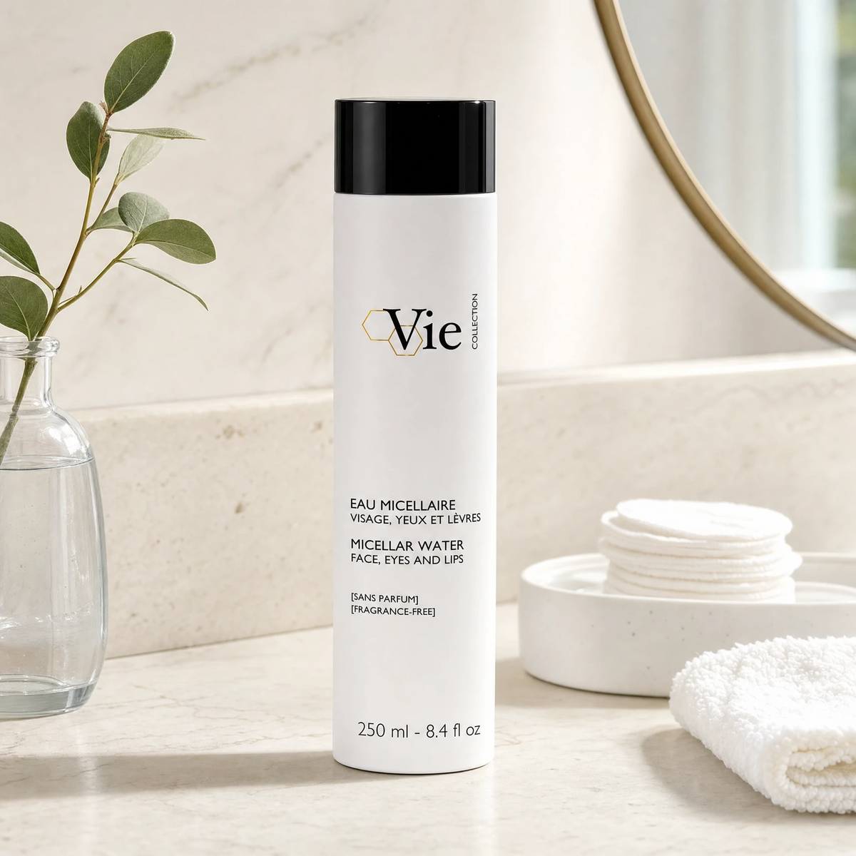 Vie Collection Micellar Water Face Eyes and Lips 250ml Fragrance-Free on a marble bathroom counter with eucalyptus in glass vase, cotton pads in ceramic dish, white waffle towel and gold round mirror, premium at-home skincare setting