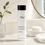 Vie Collection Micellar Water Face Eyes and Lips 250ml Fragrance-Free on a marble bathroom counter with eucalyptus in glass vase, cotton pads in ceramic dish, white waffle towel and gold round mirror, premium at-home skincare setting